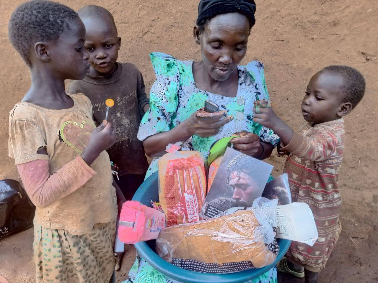 A woman stands with three children as food and gospel tracts are spread on the ground.