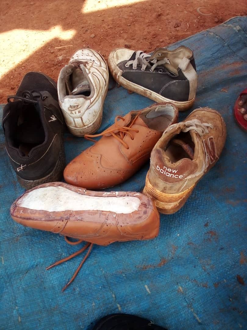 A pile of worn, mismatched shoes and boots lies on a blue tarp, showing their poor condition.