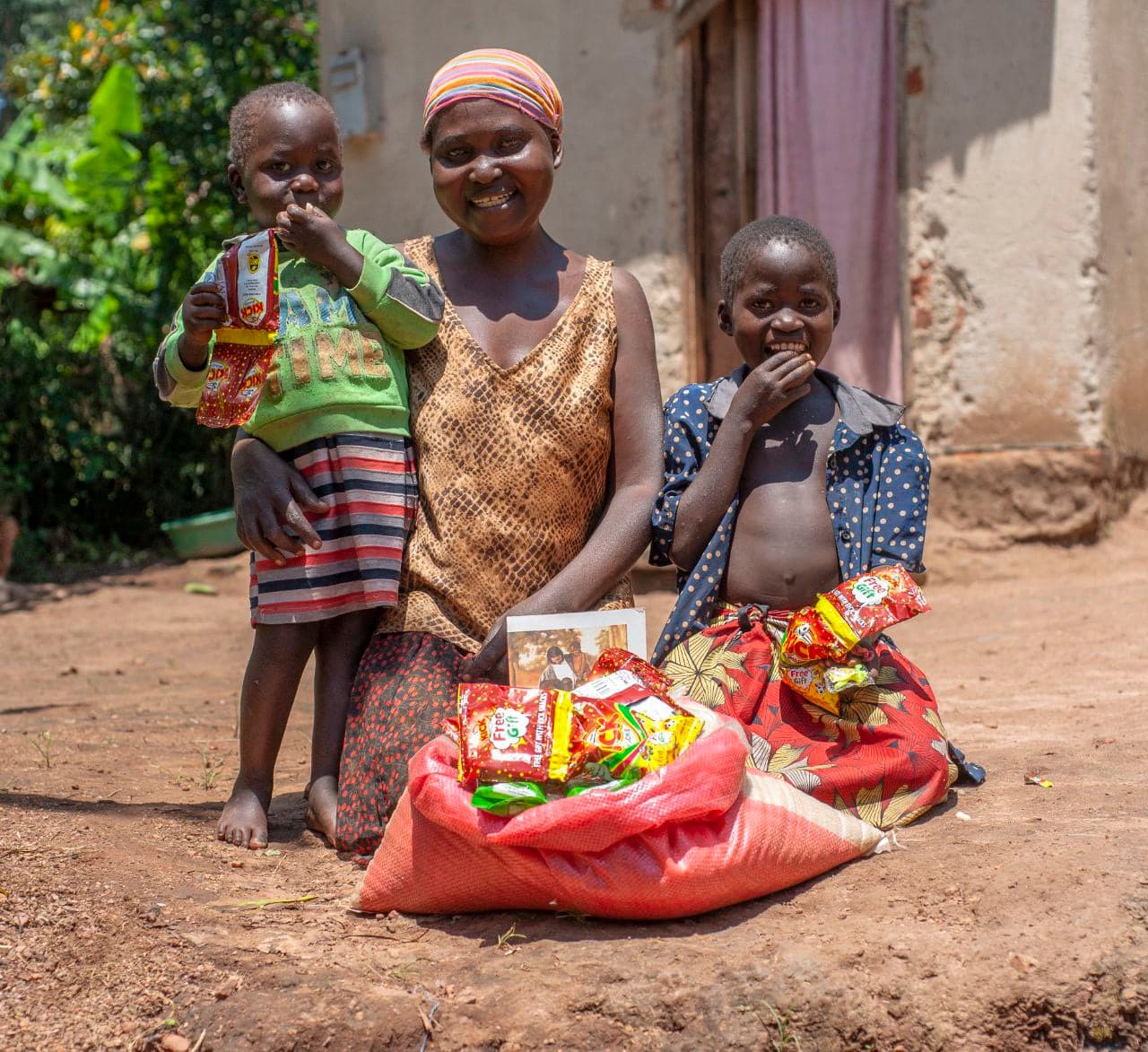 A woman stands with two children beside a large red sack of grain, one child holding a photo tract.