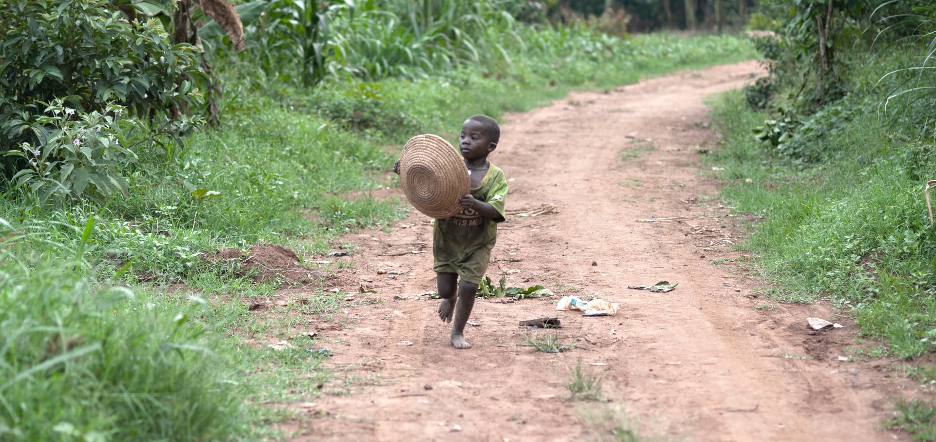 A small child walks away down a dirt path bordered by green grass.