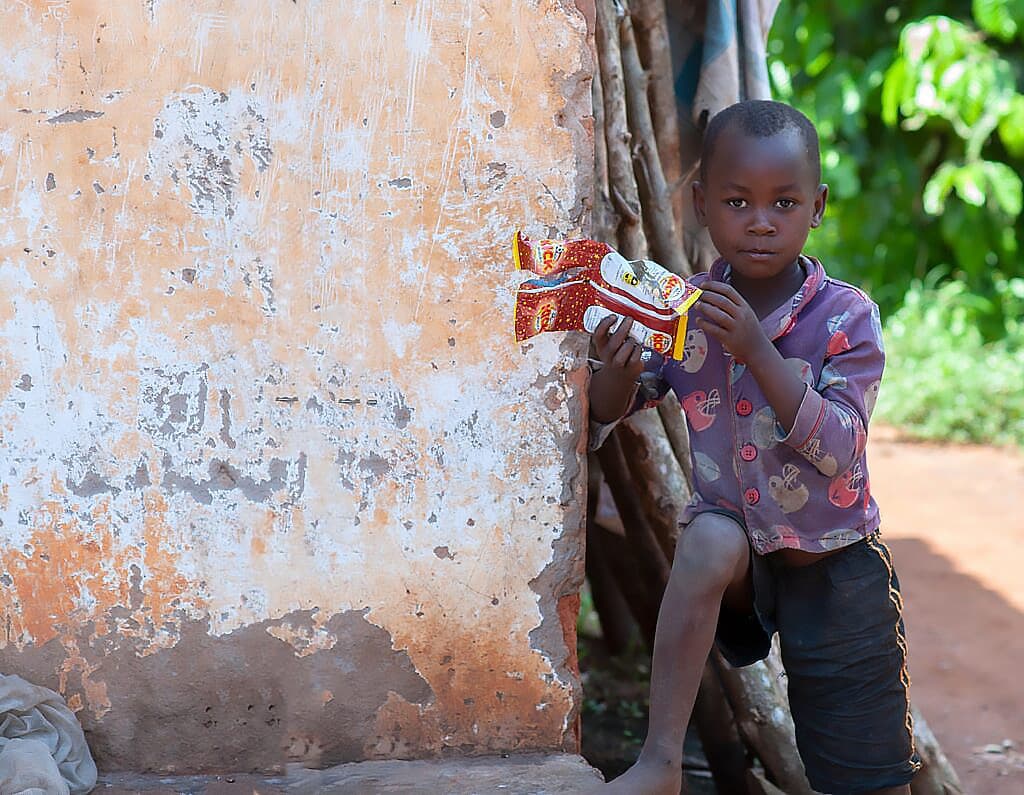 A boy sits against a weathered orange wall playing with a small toy.