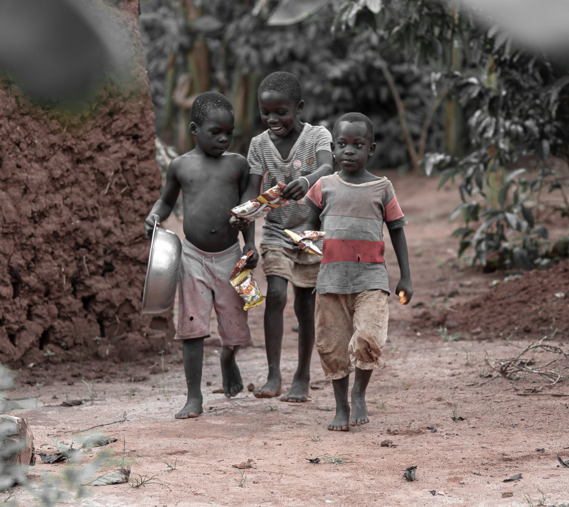 A group of children walk together along a dirt path, one carrying a bundle of clothing.