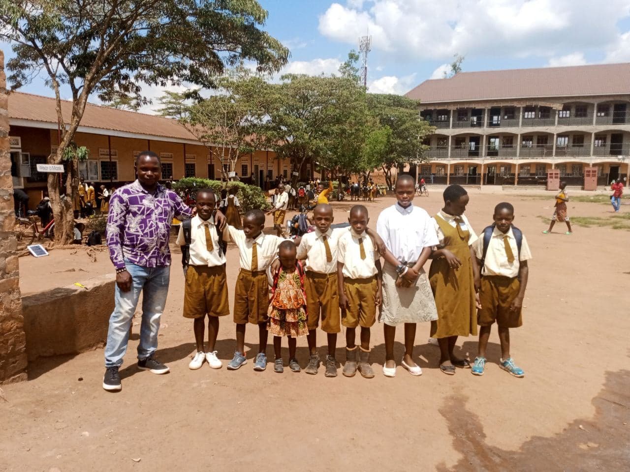 A group of uniformed schoolchildren pose outside a school building with two adults.