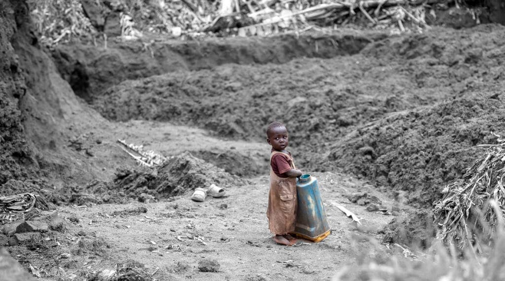 Black-and-white photo of a child standing alone in an eroded dirt quarry landscape.