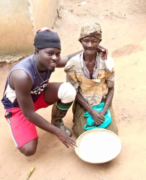 A young man kneels beside an elderly woman, both smiling as he pours something into a bowl.