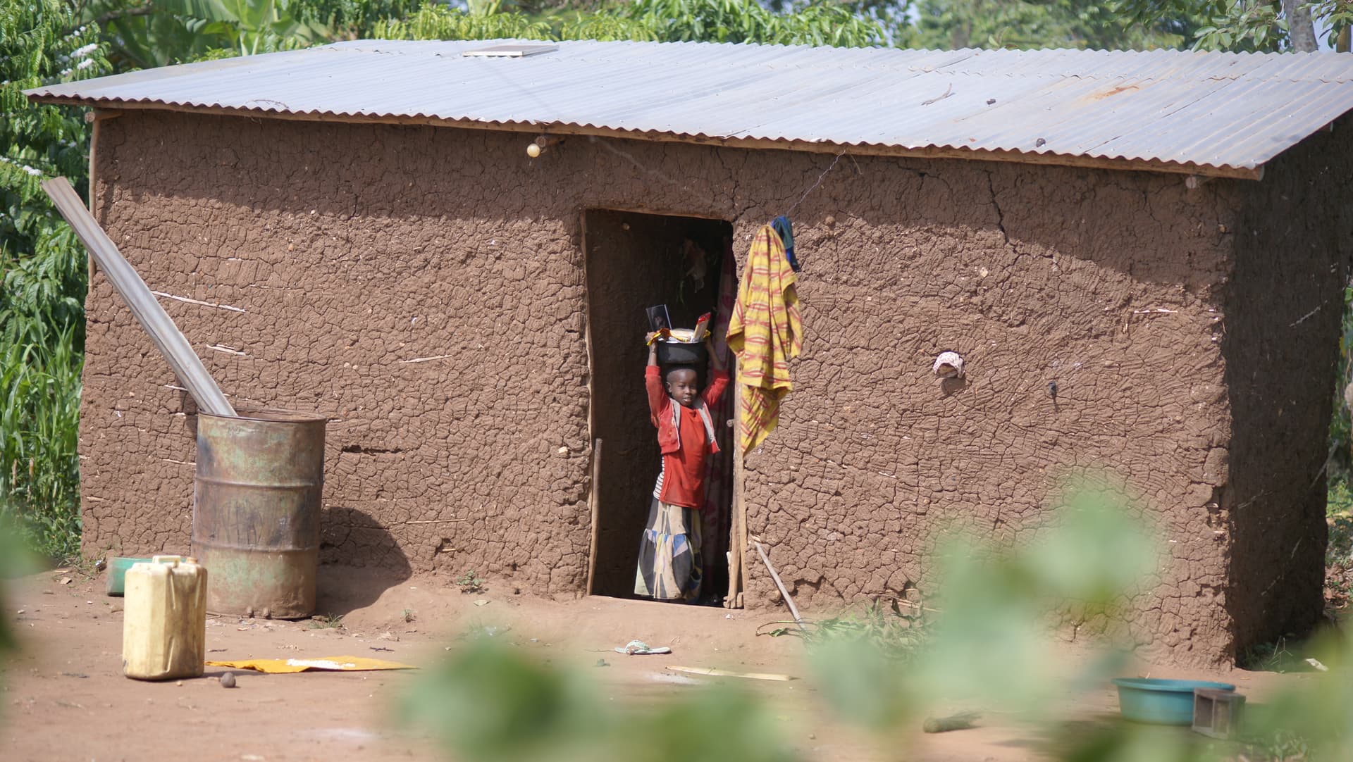 Child standing in the doorway of a mud-brick home with sacks of grain visible inside