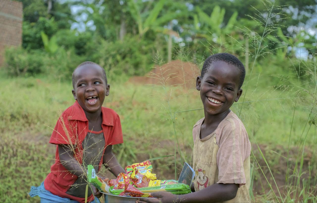 Two boys smile while holding snack packets received during a JFM food gift visit.