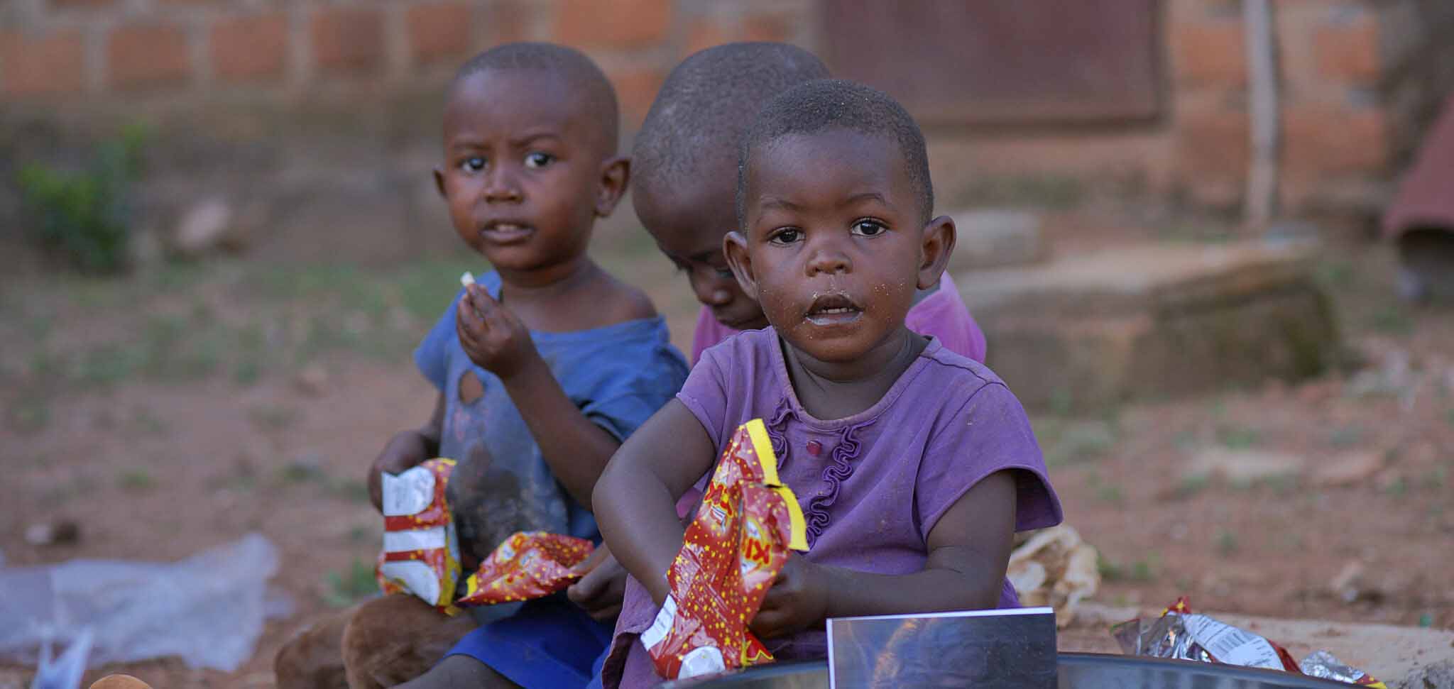 Two young children seated close together behind bowls of food during a slum food distribution