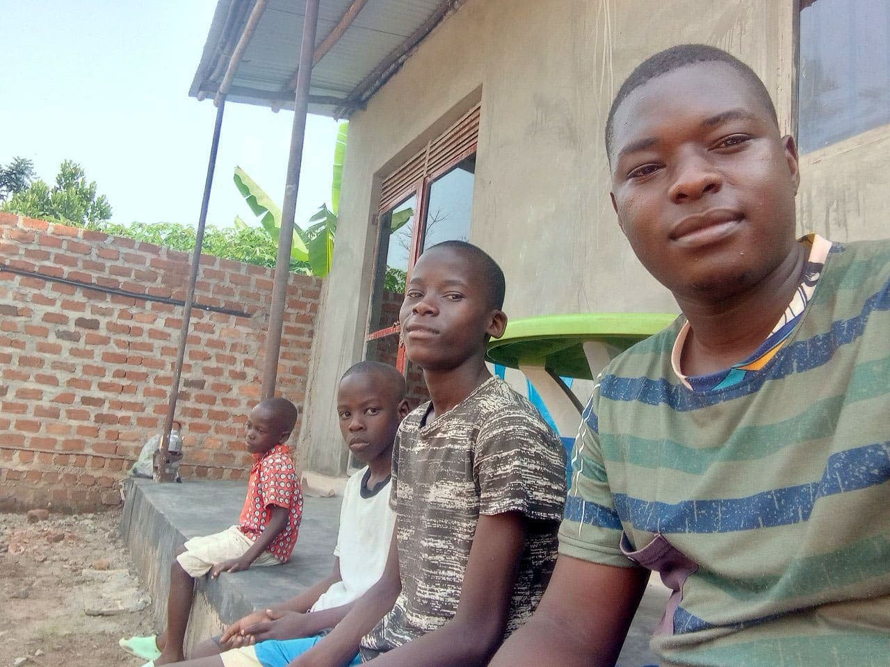 Teenage boy sitting outdoors under a covered porch with two younger children beside him