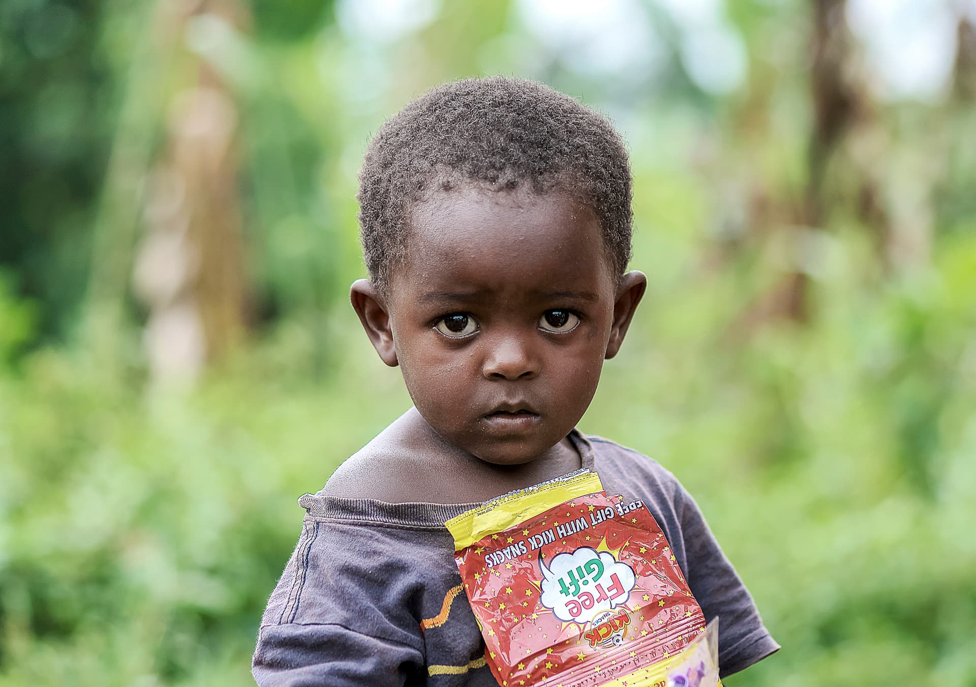 Young boy stands outdoors holding a food package against his shirt.