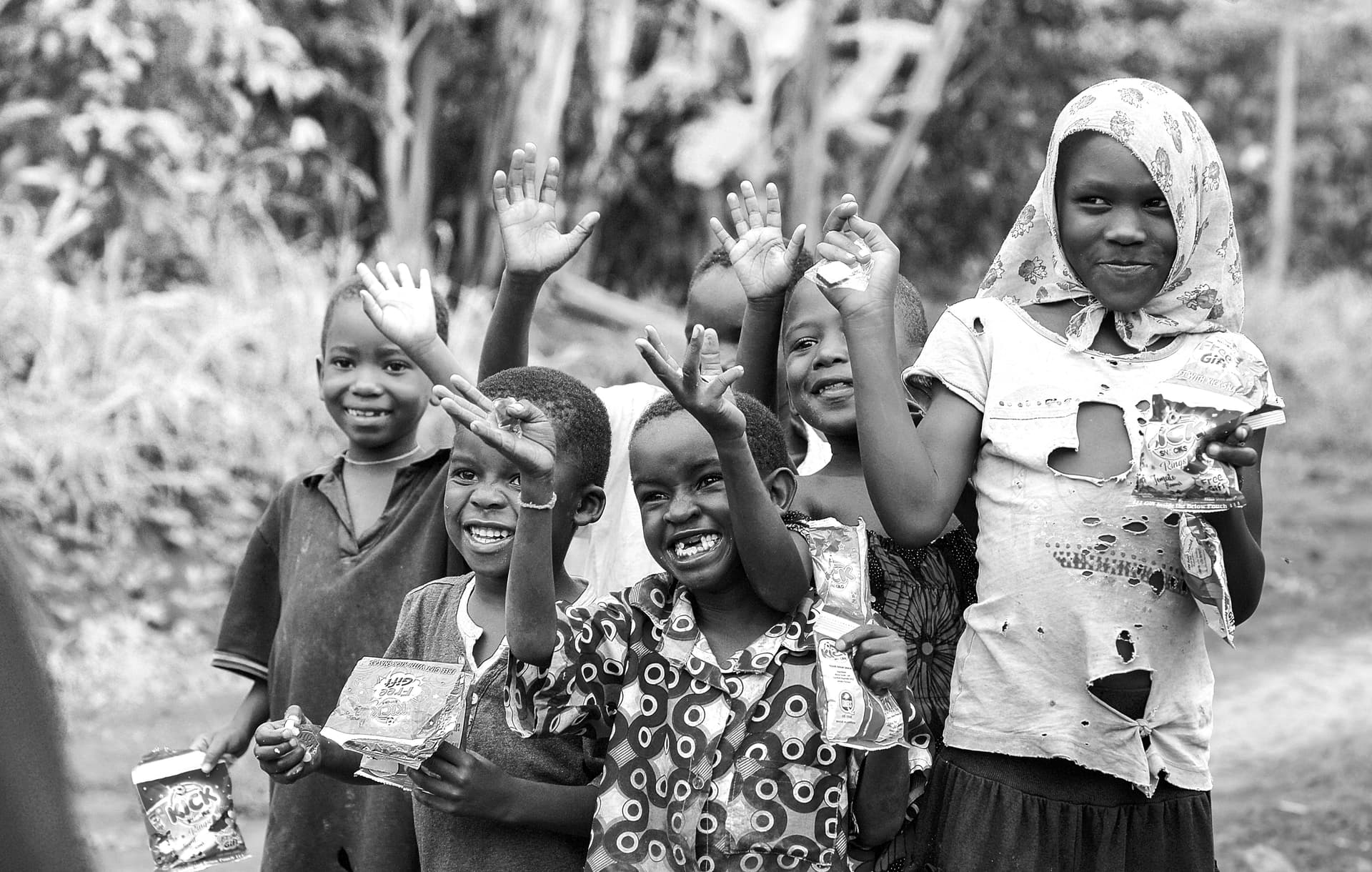Black-and-white photo of a group of children waving, an older girl in a headscarf beside them.