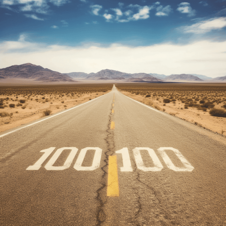 Stock photo of a long straight desert highway with '100' painted on the road, mountains in the distance.