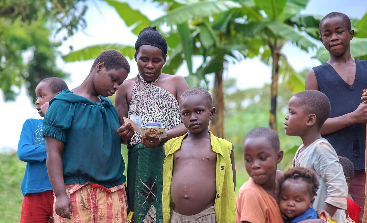 A group of children and a woman stand together outdoors near Mum Deborah's home.