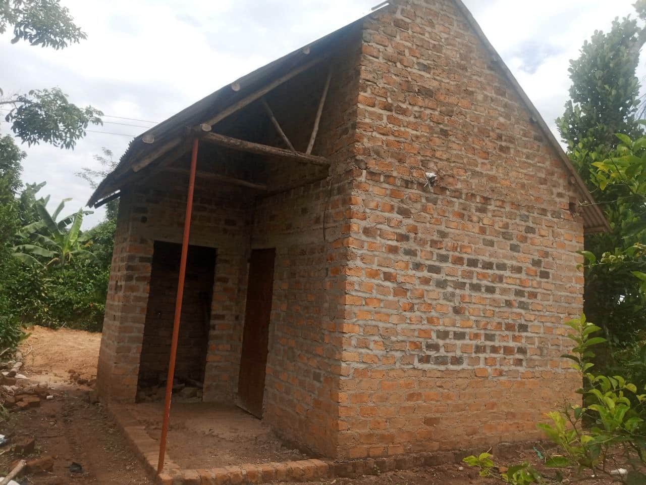 Exterior of a small red-brick house with a pitched roof under construction for Granny Kasifah.