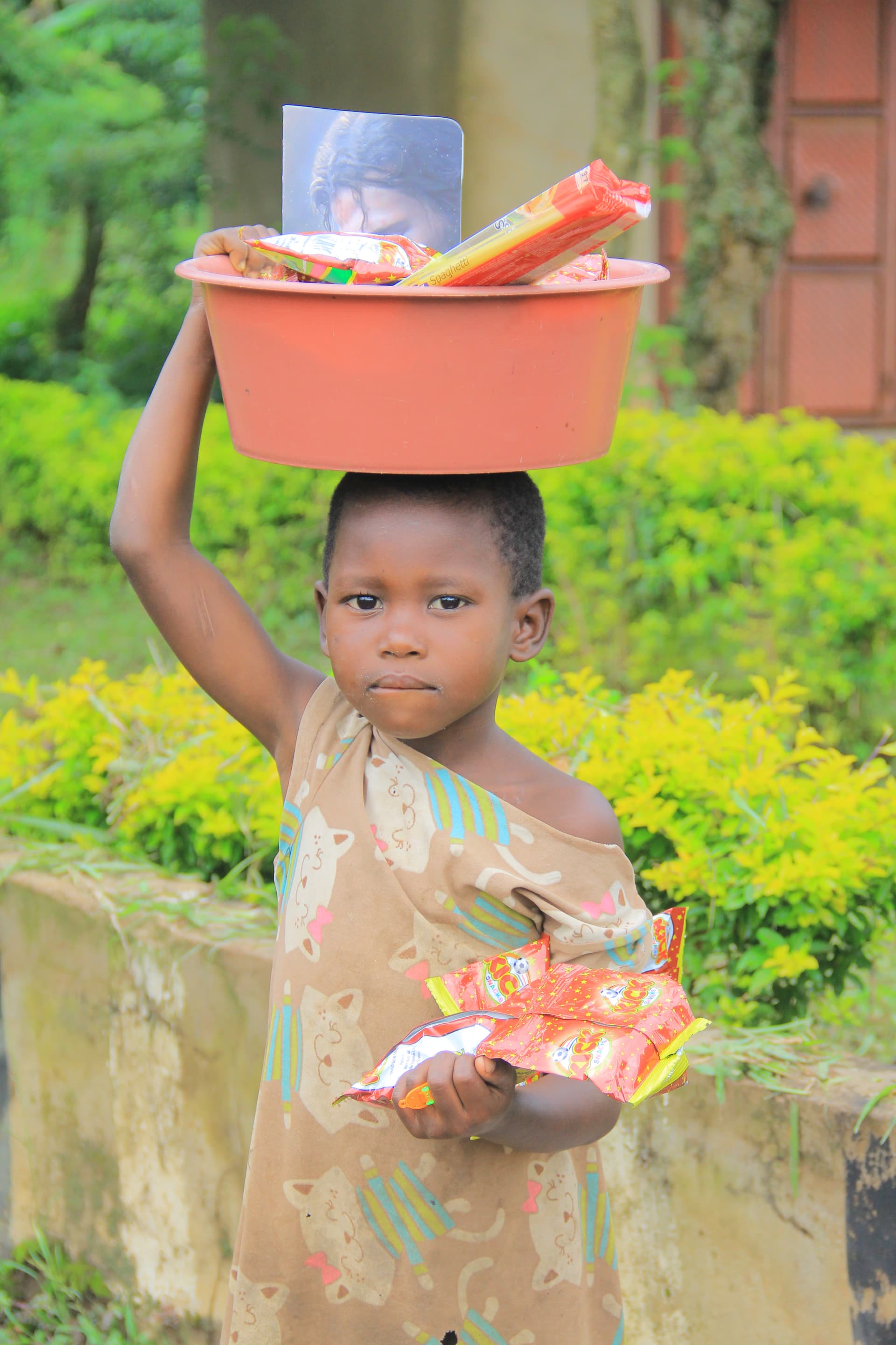 Two children stand outdoors, one holding a red JFM food gift package with a photo card.