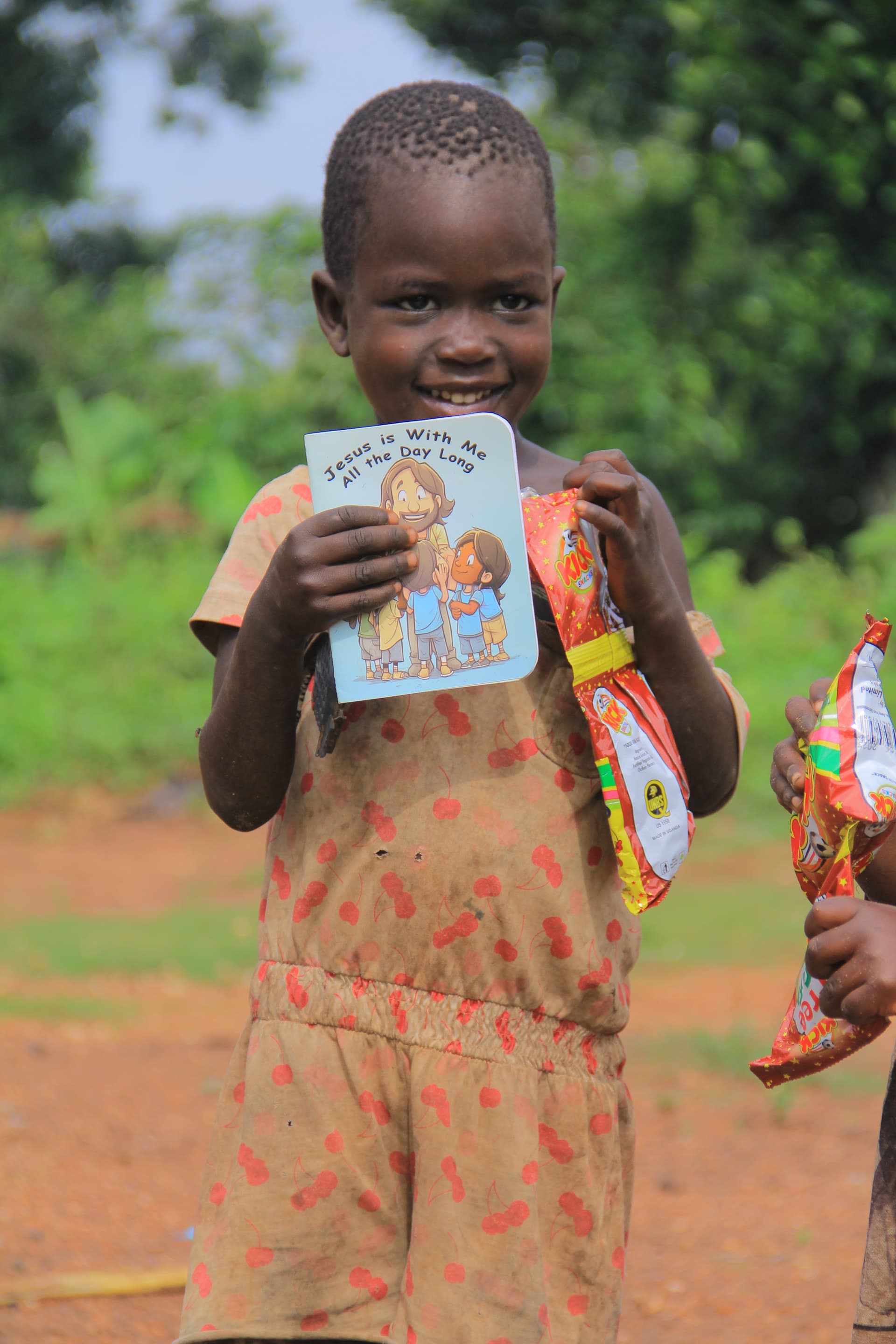 A girl in a patterned dress holds a colorful JFM food gift package outdoors.
