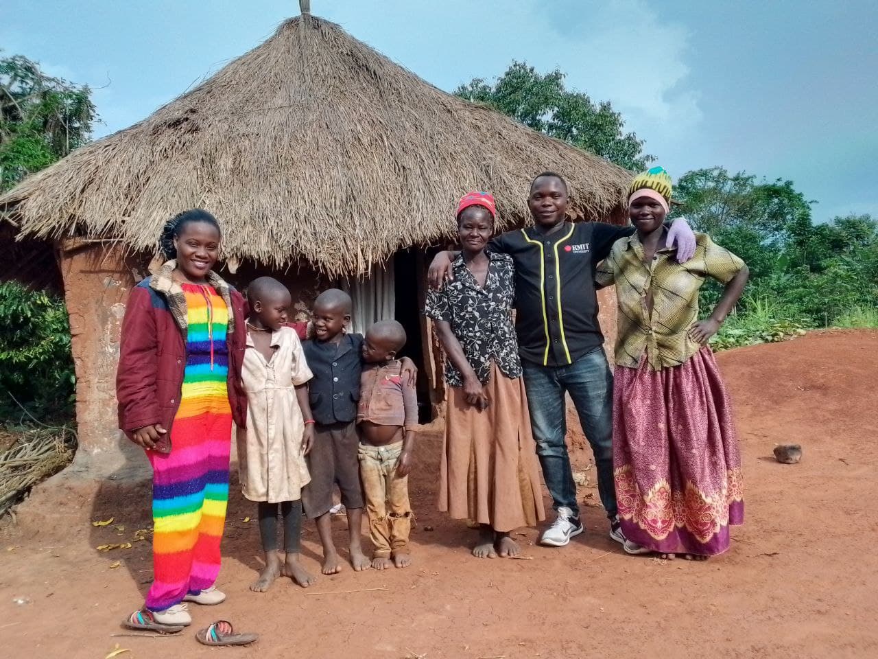 Mashariki Children's Home kids and staff pose together in colorful outfits outside a thatched-roof hut.
