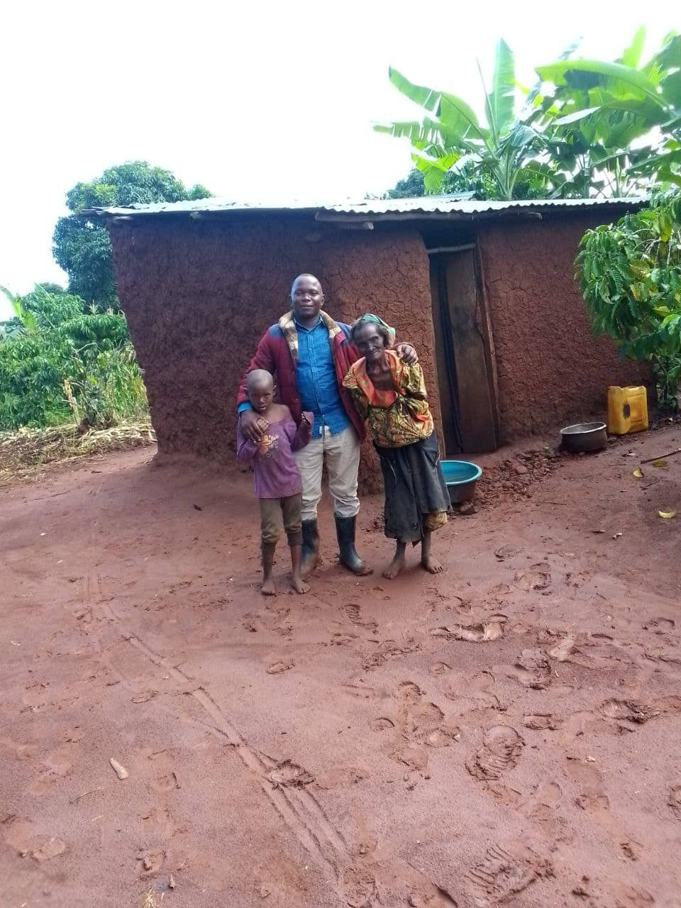 Granny Marita stands outside her mud-brick home with two grandchildren beside her.