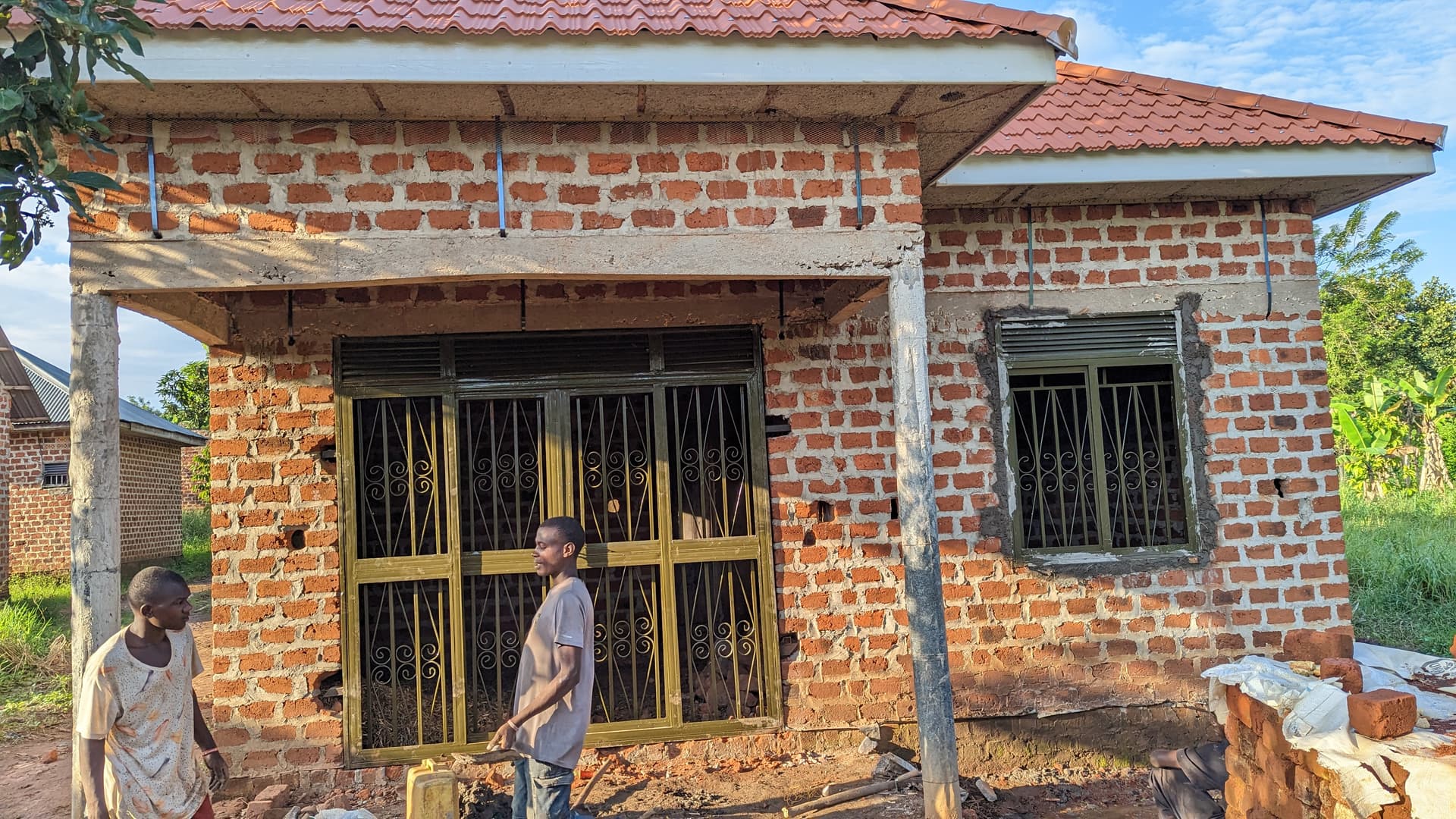 New red-brick house with an orange tile roof for Granny Maggie, a person standing beside the window.