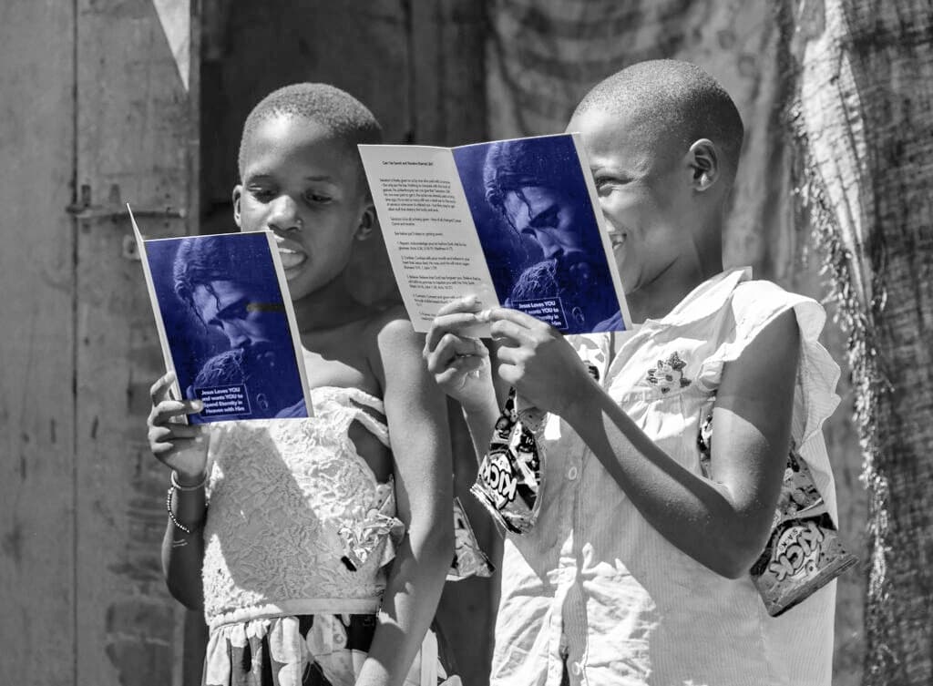 Two children stand outdoors reading open blue booklets together, shown in a desaturated toned photo.