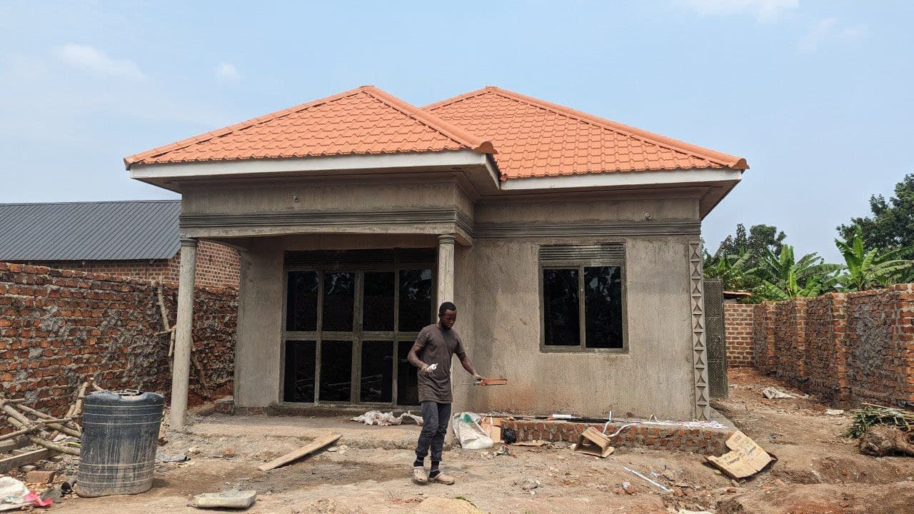 Newly built house with an orange tiled roof and unplastered walls, a man standing near the entrance.