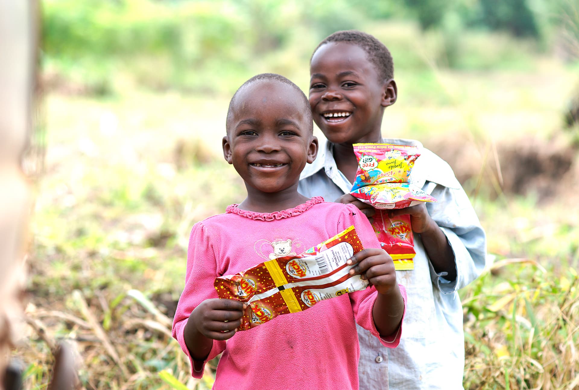 Two smiling boys stand together outdoors, each holding a gospel tract booklet.