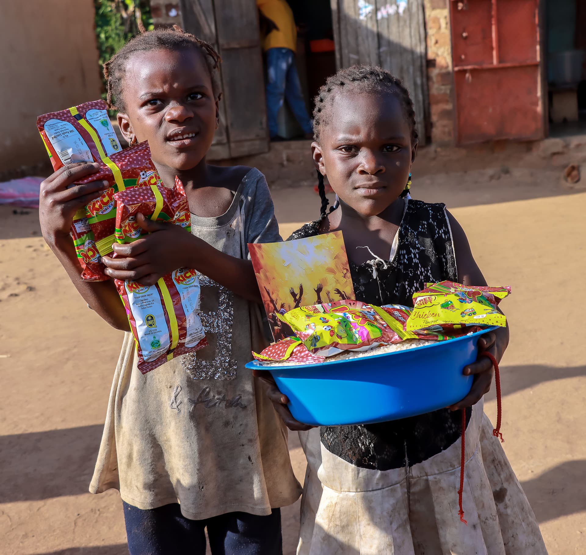 A woman and a girl stand outdoors holding gospel tract booklets and a blue basin.
