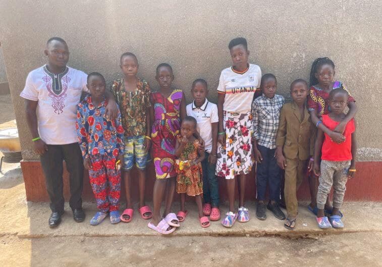 Group photo of a man and children in colorful clothes standing together outside at Mashariki Children's Home.