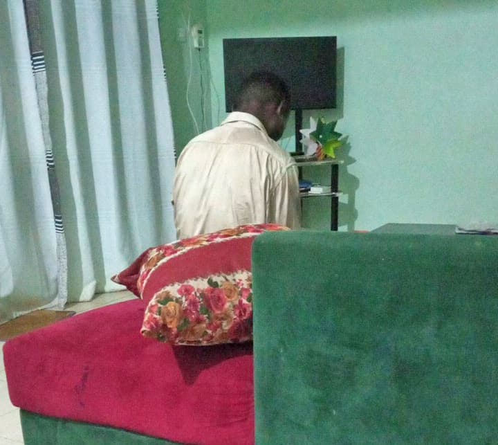 Low-quality photo of a man seated with his back to the camera in a room with teal walls.