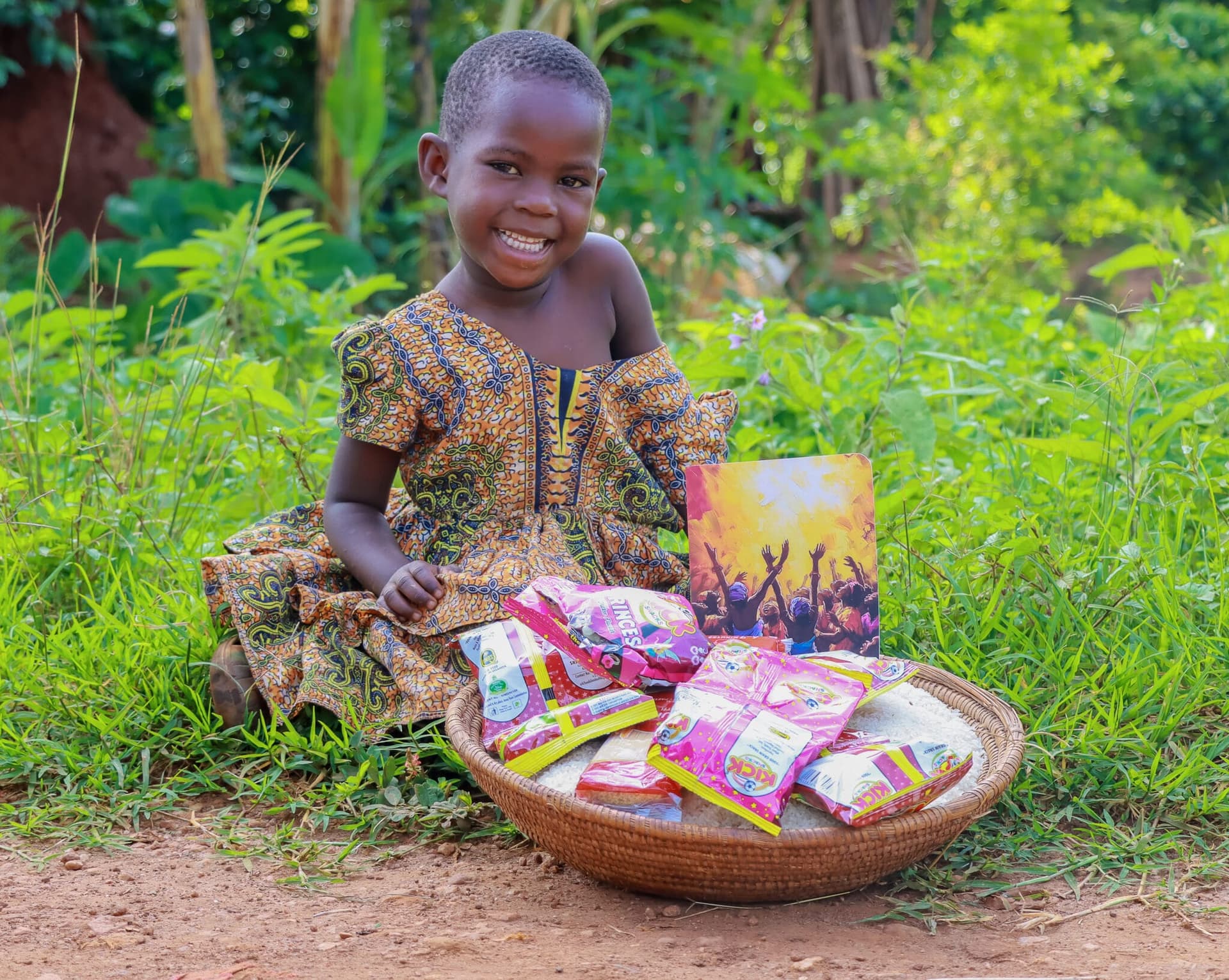 Girl sitting on the ground outdoors holding a wooden bowl full of snack packets and a gospel tract.