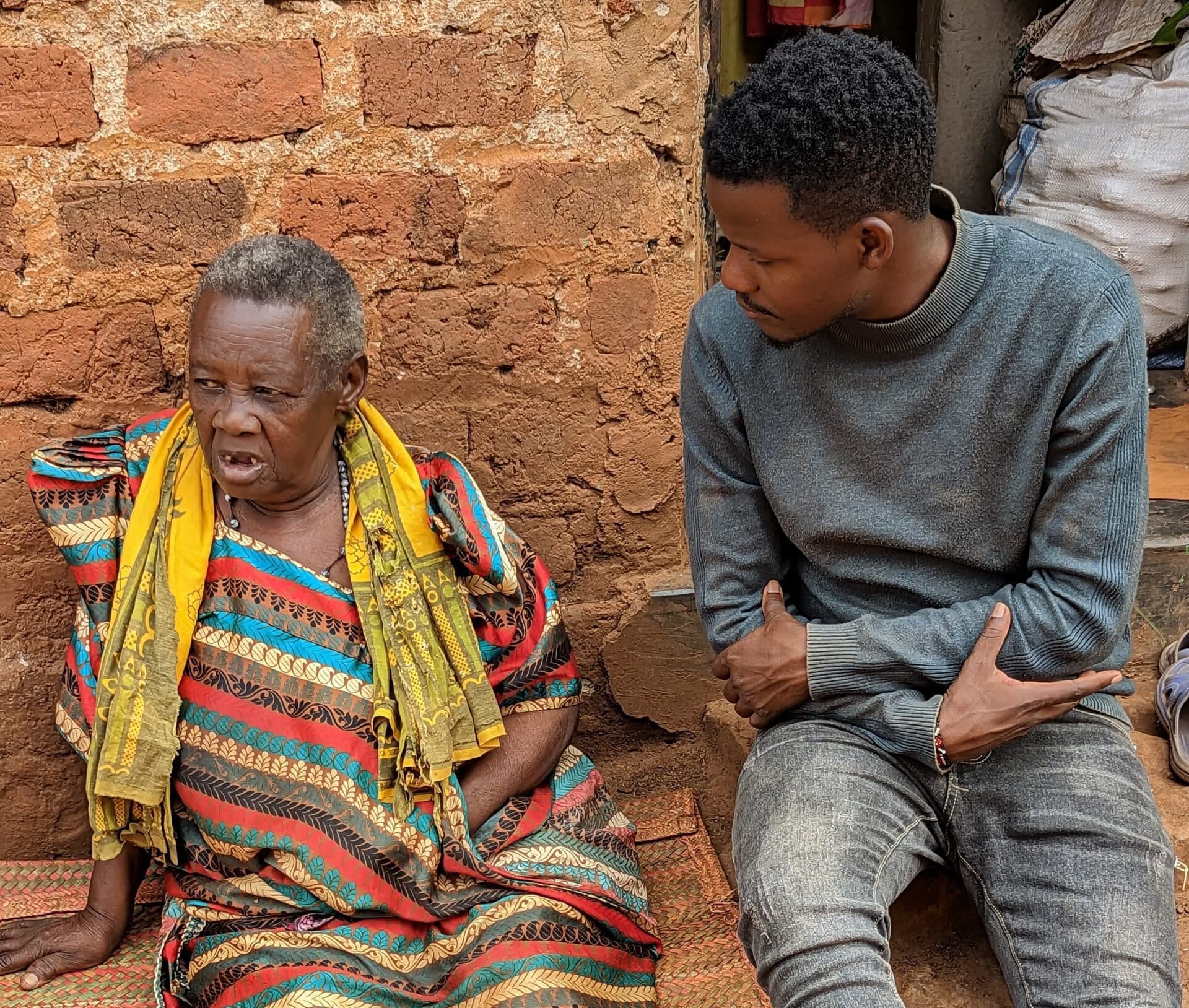 Elderly woman in a striped shawl gesturing while talking with a young man seated beside her.
