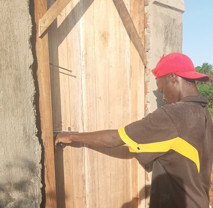 A man in a red cap builds a wooden door frame for the pit latrine at Miracle Medical Center.
