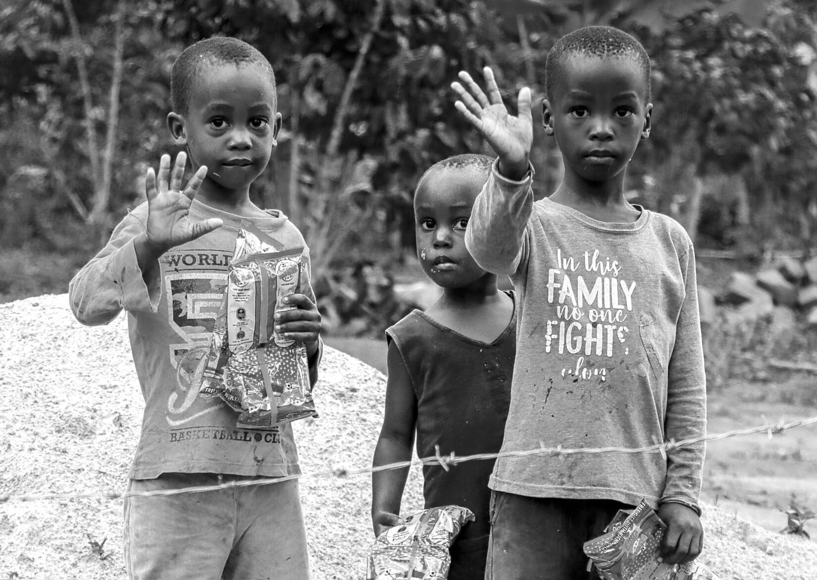Black-and-white photo of two children waving at the camera outdoors, one wearing a graphic T-shirt.