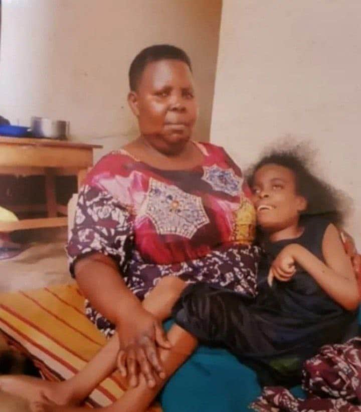 Woman sitting indoors holding Sarah, a young woman with cerebral palsy, on her lap