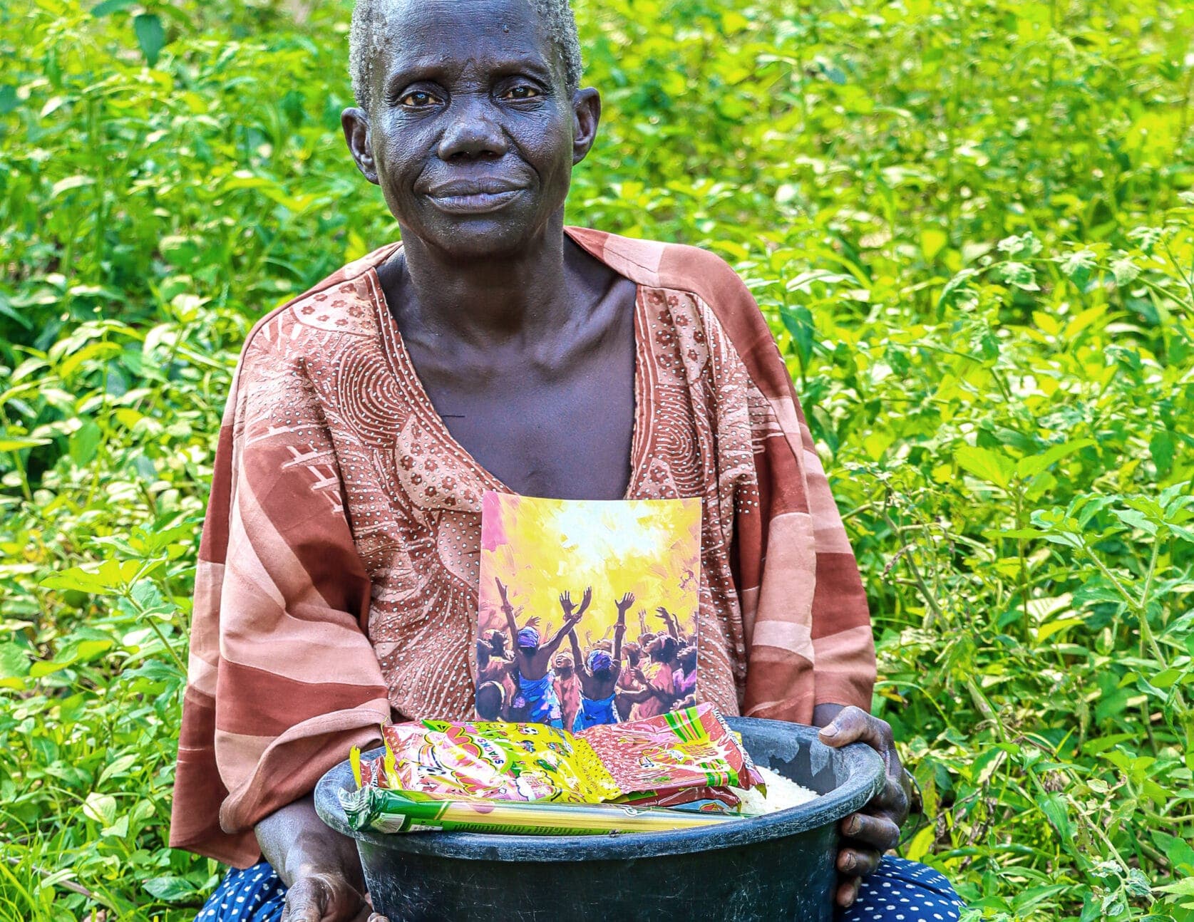 Elderly woman, likely Elder Annet, standing in a green field holding a gospel tract and gift bowl.