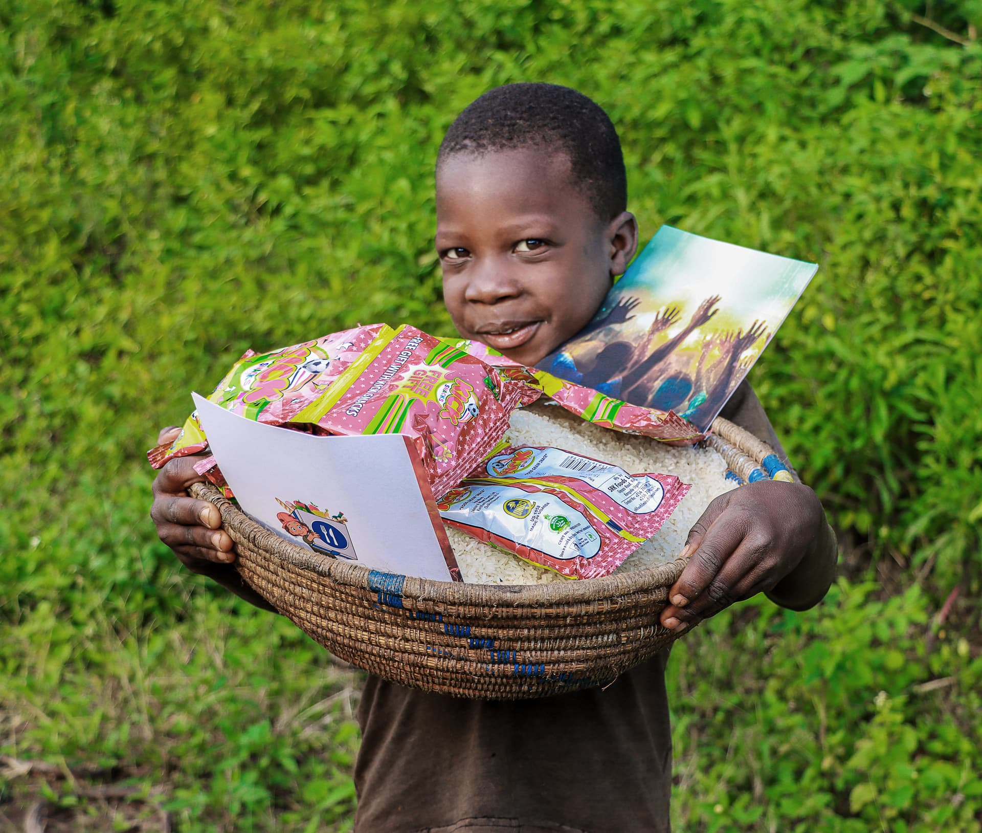 Boy smiling while holding a basket of snack packets and a picture book