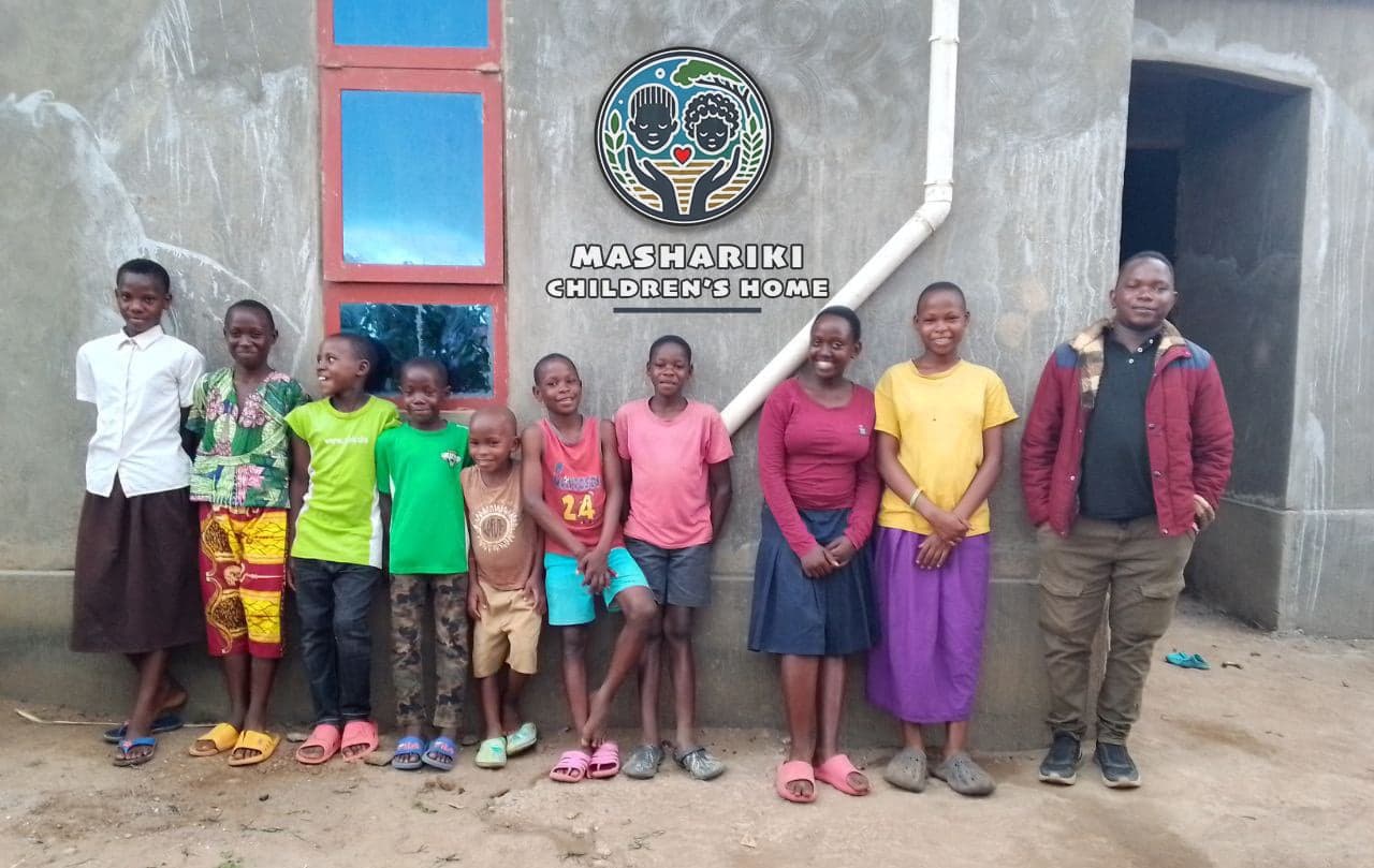Group of children and a man in a red shirt posing outside the Mashariki Children's Home building