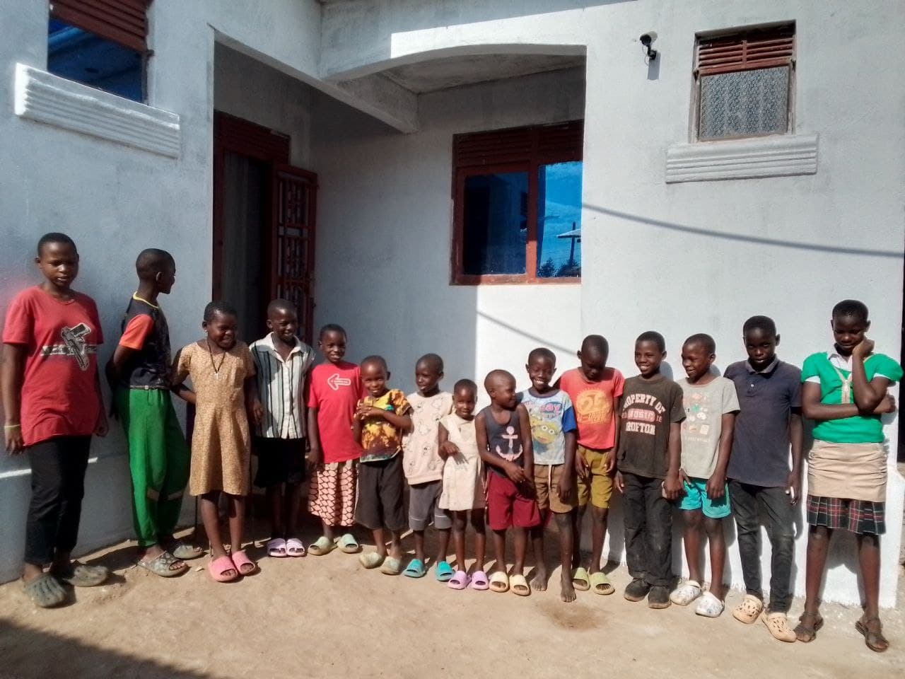 About ten children from Mashariki Children's Home pose together outside a white building.