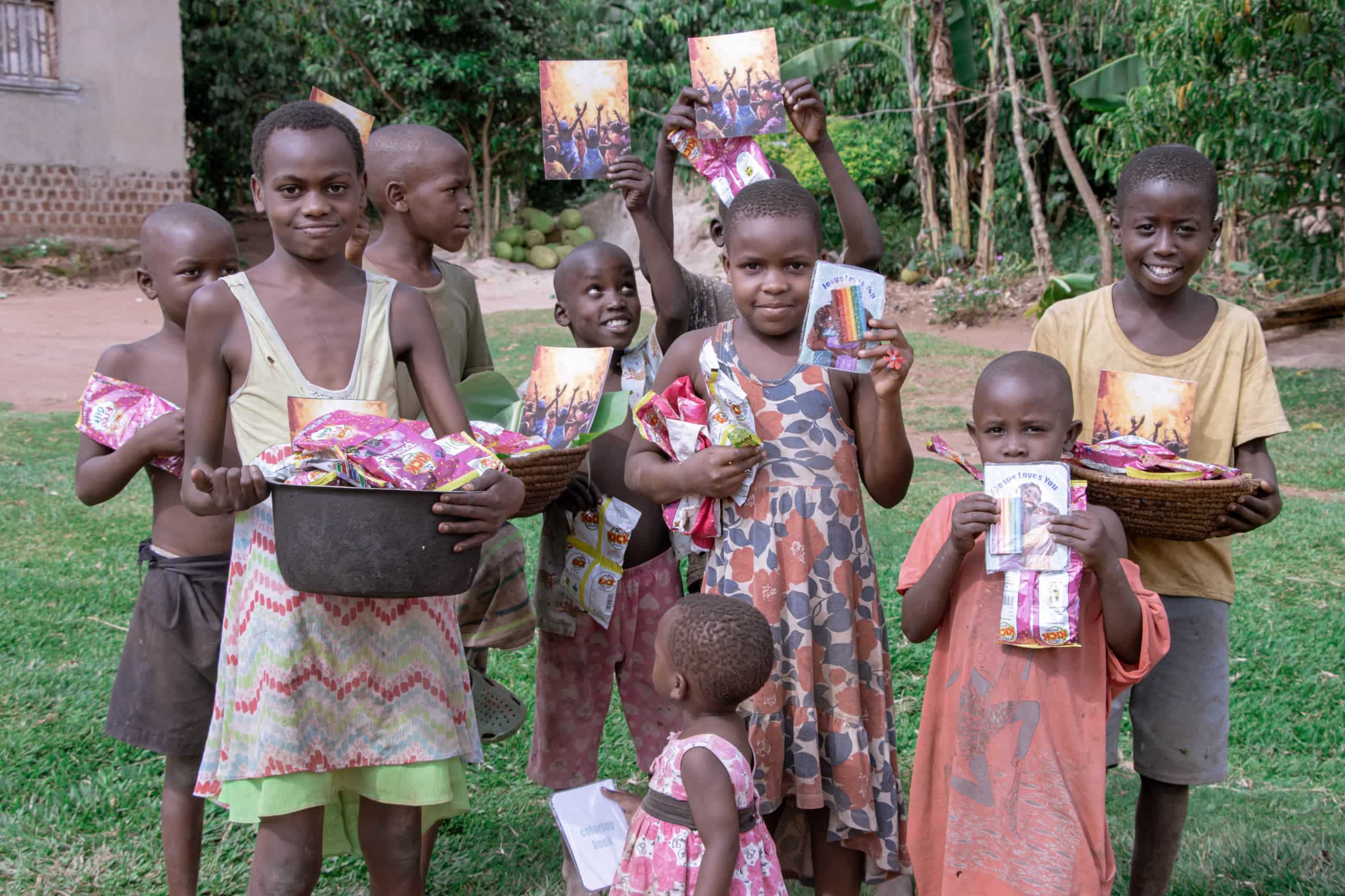 Group of children standing outdoors, each holding a food packet, one balancing a basin on her head.