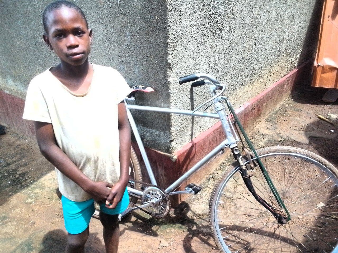 Travis stands beside an old bicycle in front of a rusty metal wall.