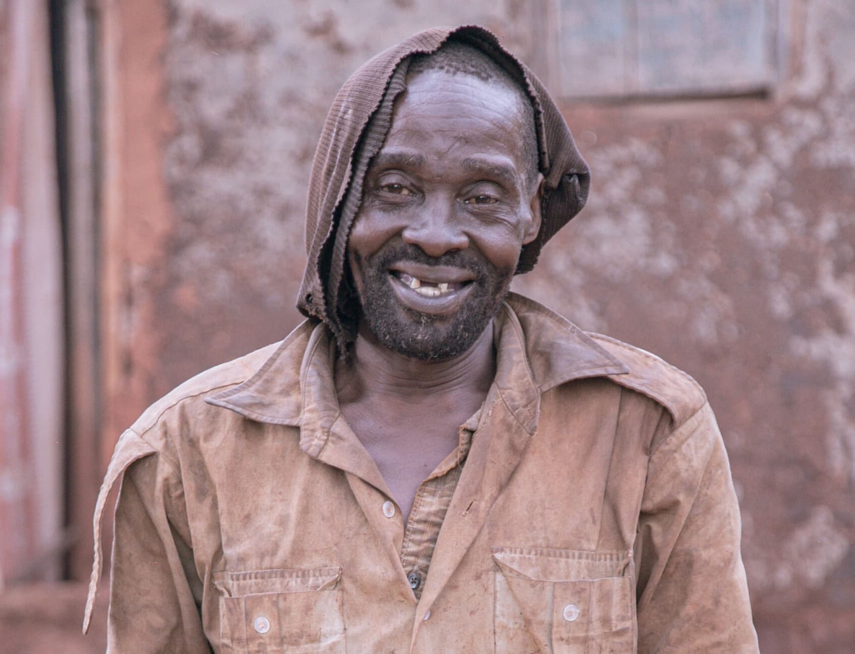 Close-up portrait of a smiling man wearing a tan collared shirt outdoors.