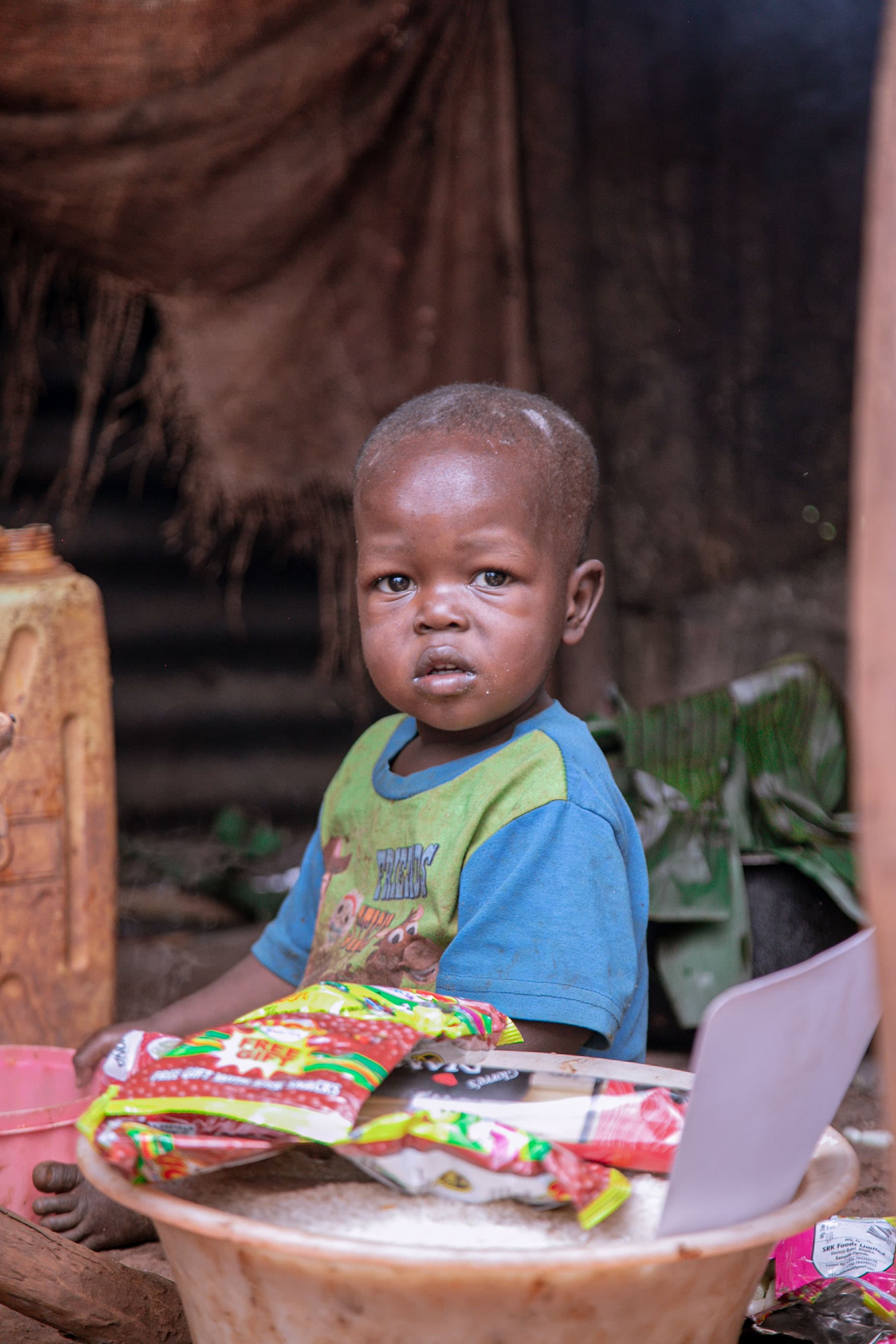 Toddler boy sitting at a table with food packets in a sheltered outdoor setting.