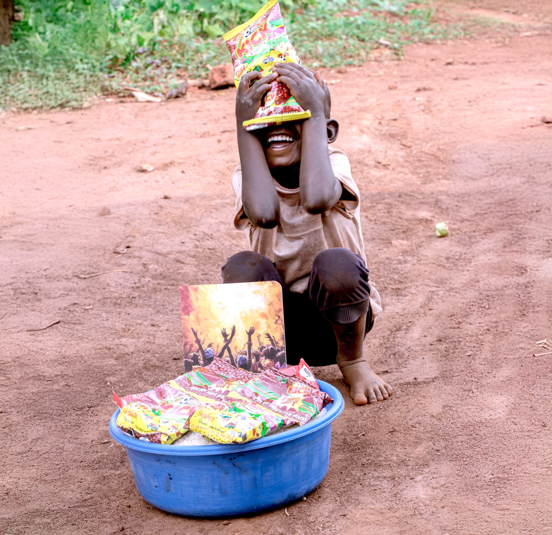 A mother and child laughing together outdoors, the child holding a food gift packet.