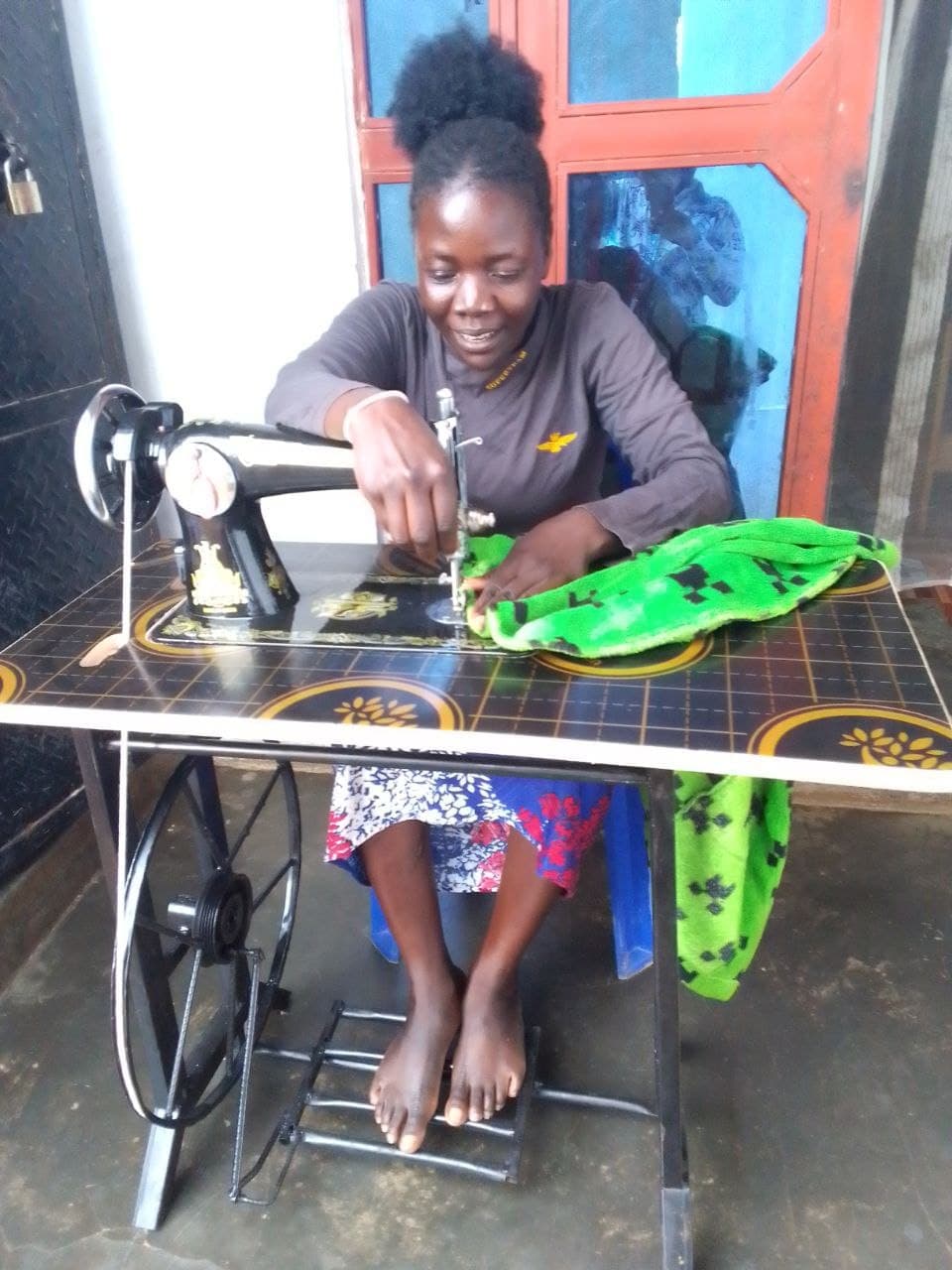 Hashinat smiles while sewing green fabric on a treadle sewing machine.