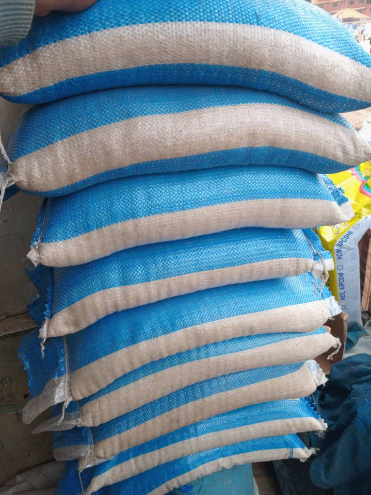 Stacked sacks of grain wrapped in blue and tan woven bags at a food store.