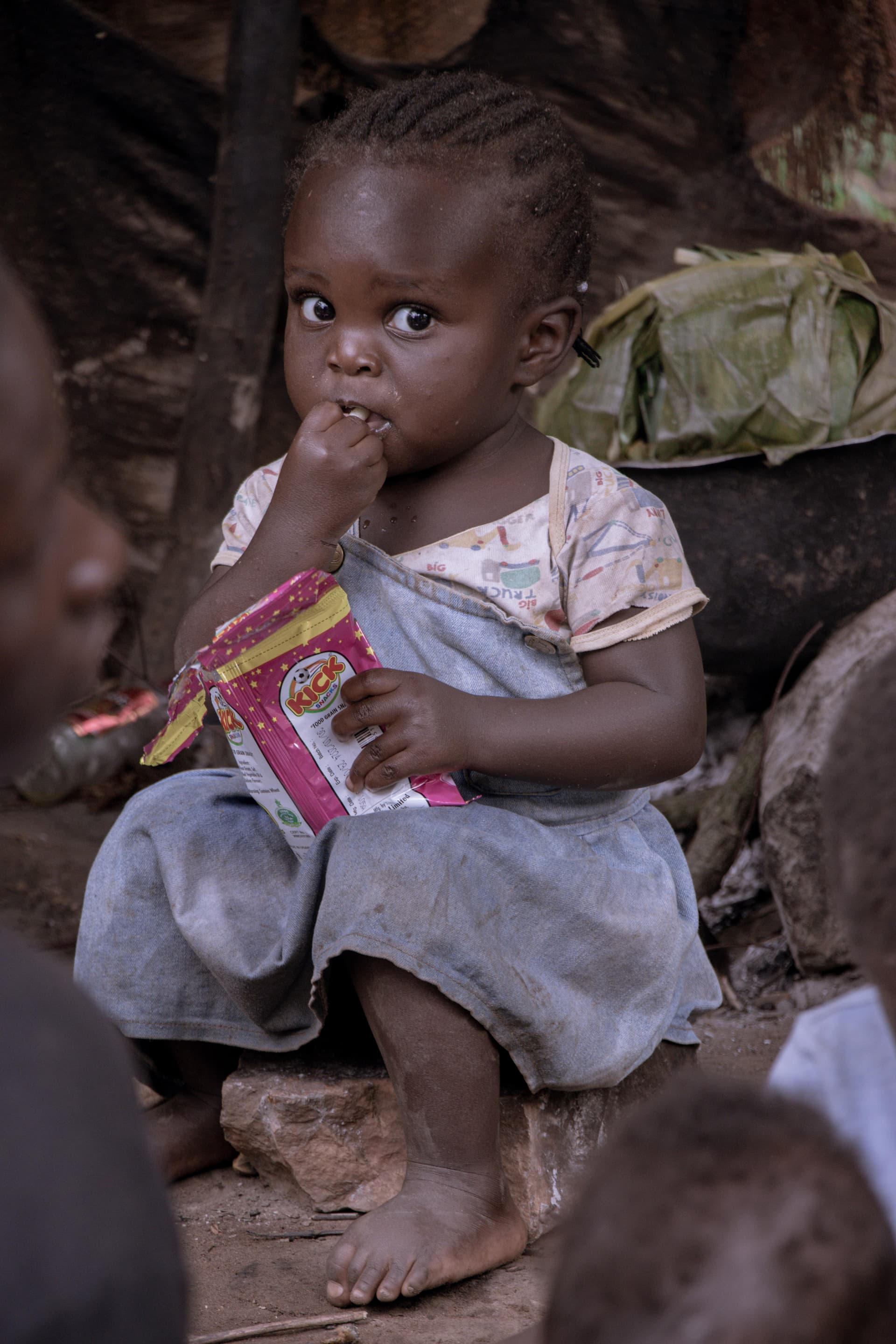 A young child seated outdoors, eating a food gift snack.