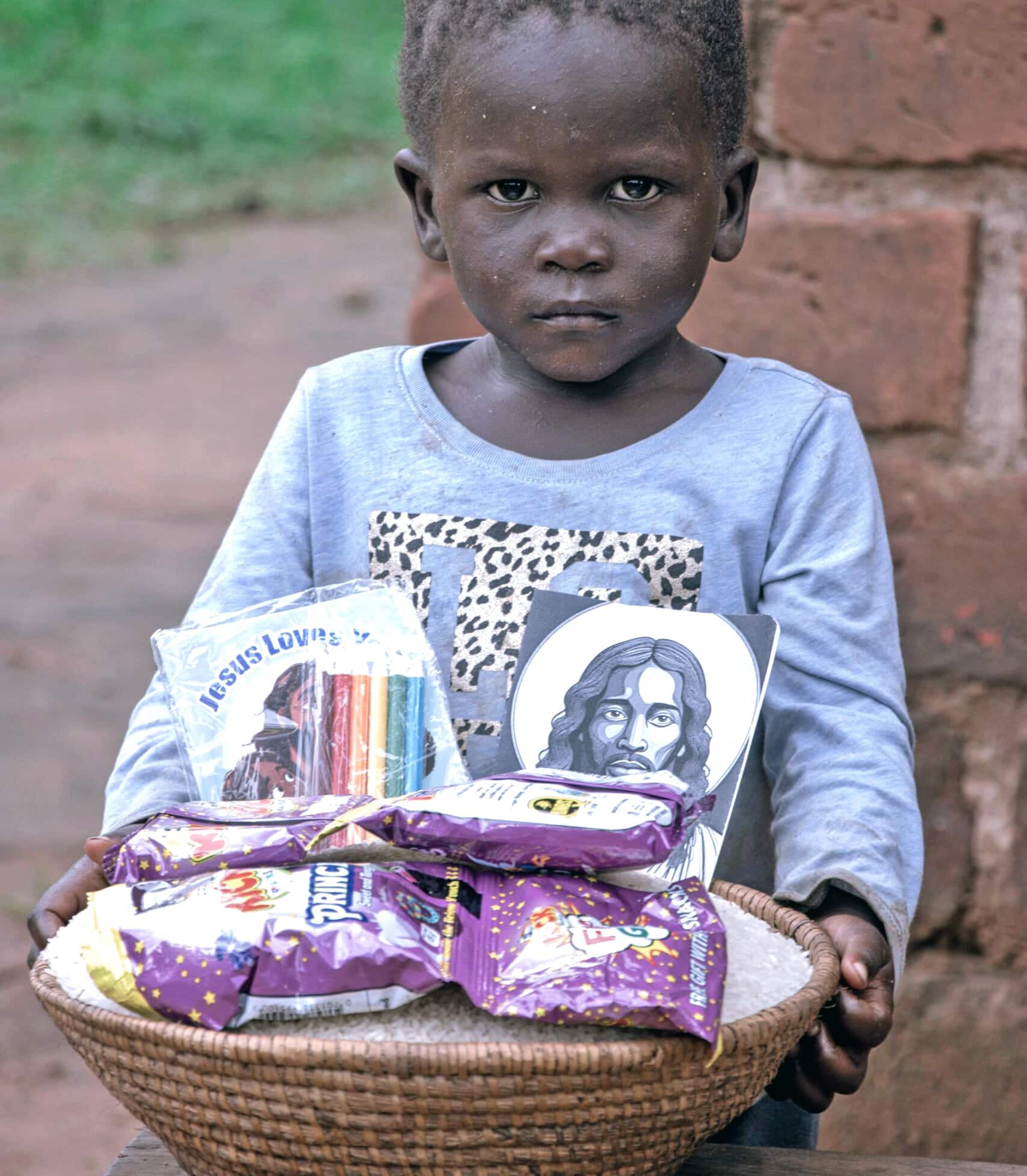 A young child seated with a basket of food gift packets.