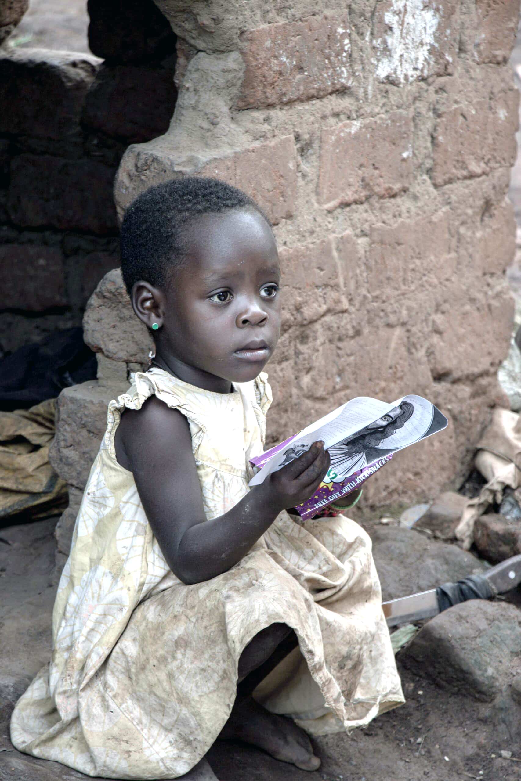 Young girl seated on the ground holding a gospel tract.