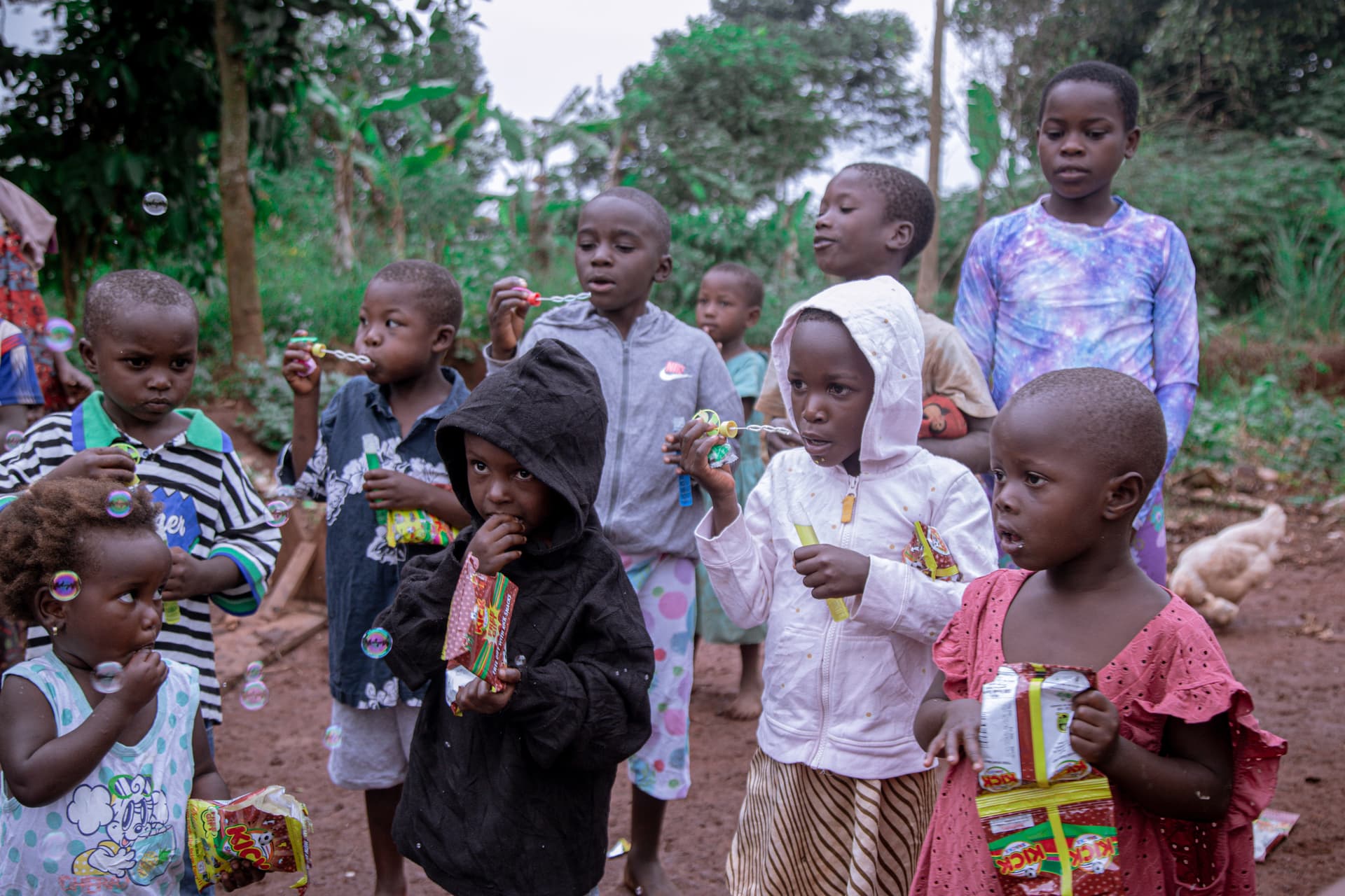 Group of children in new clothing gathered outdoors, one boy in front holding a food packet.