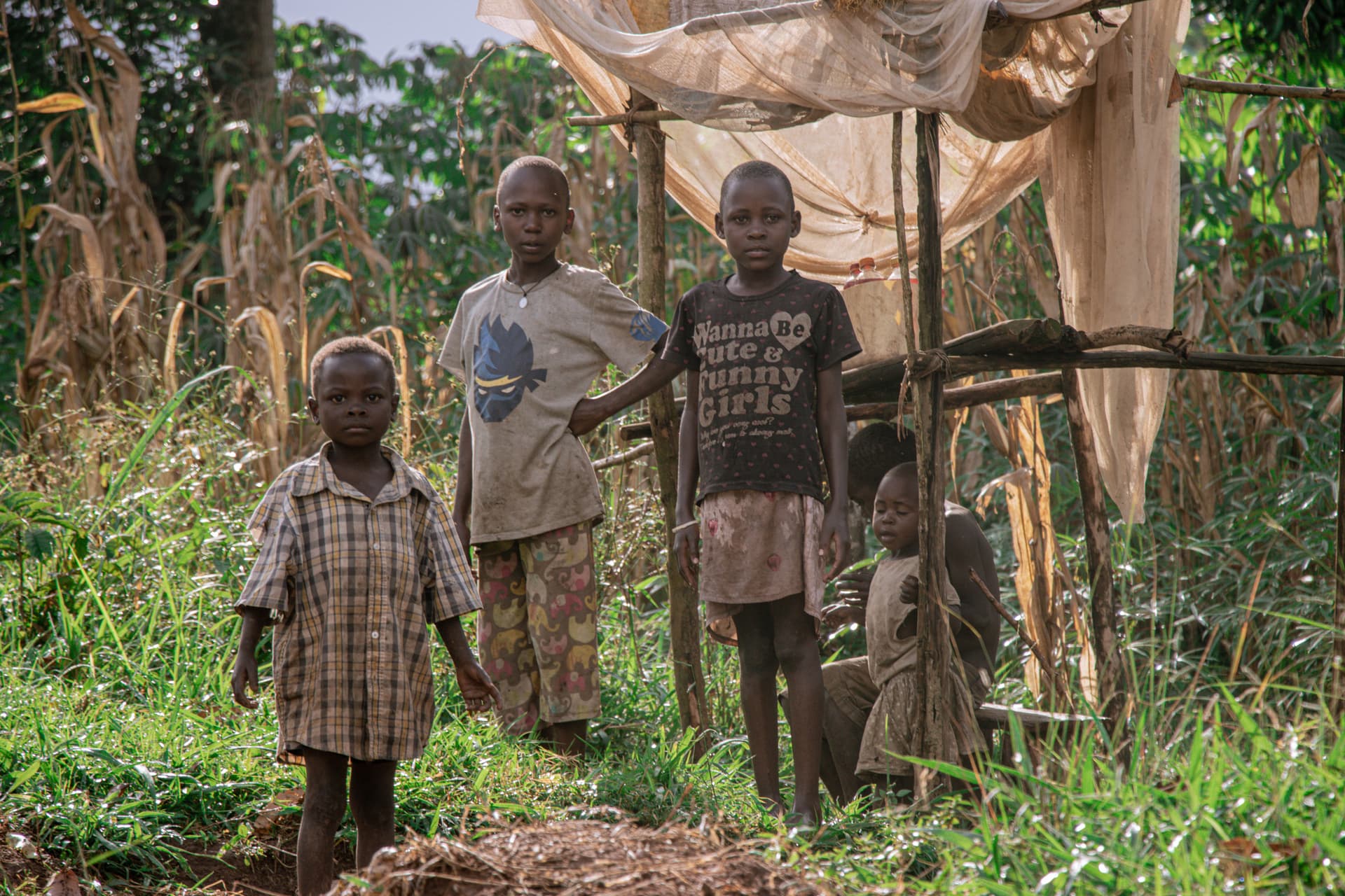 A group of children standing together outdoors near tree branches and vines.